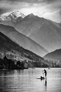 Man with dog paddleboarding in lake against mountain range