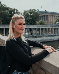 Young woman looking away while standing by retaining wall in city