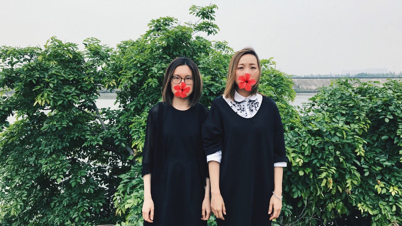 young women, real people, front view, two people, lifestyles, young adult, leisure activity, looking at camera, traditional clothing, togetherness, black color, tree, teenage girls, standing, portrait, plant, outdoors, green color, day, women, smiling, bonding, friendship, sky