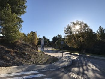 Empty road by trees against blue sky