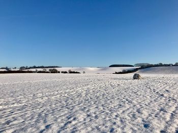 Snow covered landscape against clear blue sky