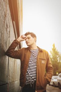 Young man looking away while standing against wall