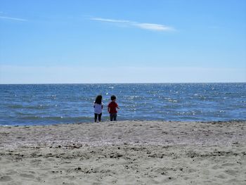 Rear view of siblings standing at beach against sky