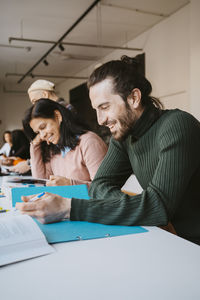 Smiling young man studying by female friend at community college