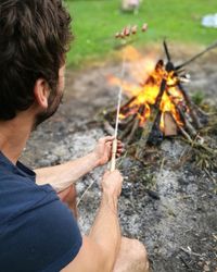 Man holding sausage in stick over bonfire