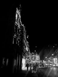 People on illuminated buildings in city against sky at night