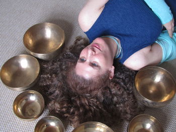 High angle view of young woman lying by singing bowls on mat