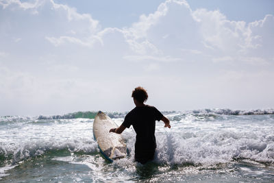 Rear view of man with surfboard in sea
