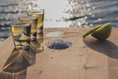 Close-up of tequila shots with lemon on table by sea