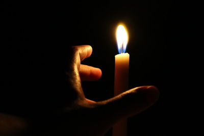 Cropped hand holding lit candle in darkroom
