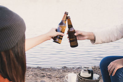 Friends toasting beer bottles at lakeshore