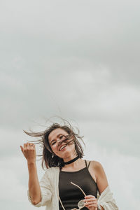 Young woman smiling while standing against sky