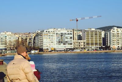 Rear view of people by river against buildings in city