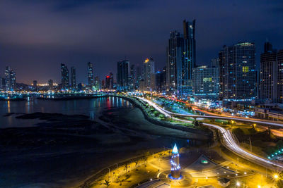 High angle view of light trails on road in illuminated city by river at dusk