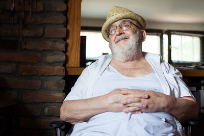 Thoughtful senior man looking away while sitting on chair at home