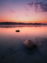 Scenic view of rock in lake against sky during sunset