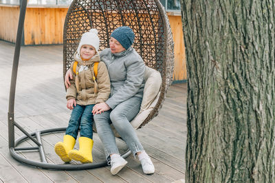 Grandmother and granddaughter sat down to rest after a walk in a hanging rattan chair outdoors