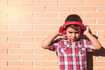 Cheerful boy listening music while standing against wall