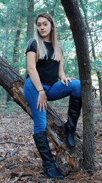Portrait of young woman sitting on tree trunk in forest