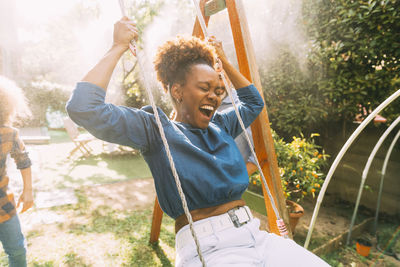 Happy woman with eyes closed swinging in backyard