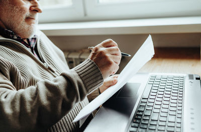 An elderly man works at a laptop, learning from home, home bookkeeping