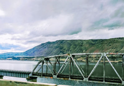 Bridge over river by mountain against sky