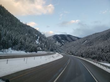 Road by snowcapped mountains against sky during winter