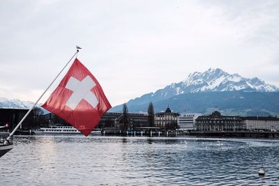 Swiss flag by river against mountain and sky during winter