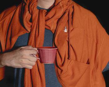 A dark pink mug being holded by a person in orange top.