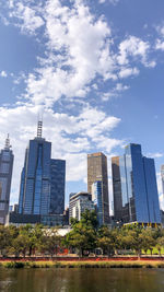 Modern buildings by river against sky in city