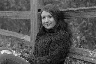 Portrait of smiling girl sitting by wooden railing during autumn