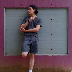 Young man looking away while standing against wall. grey tones with pink accent
