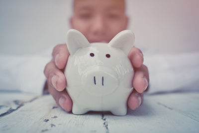 Portrait of boy holding piggy bank on table at home