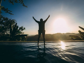 Silhouette man standing at riverbank against sky