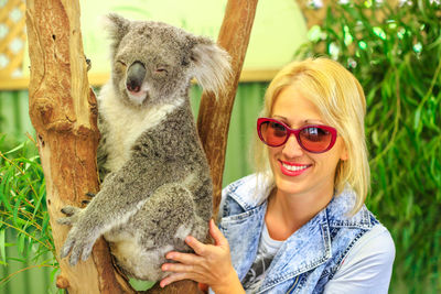 Portrait of smiling young woman with koala by tree trunk