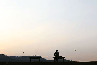 Silhouette man standing on street against sky during sunset