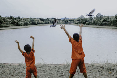 Rear view of boys with arms raised standing by lake