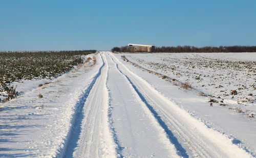 Tire tracks on snow field against clear blue sky