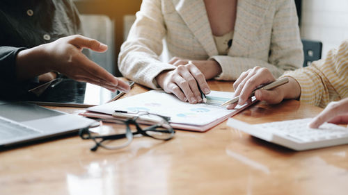 Midsection of woman holding smart phone while sitting on table