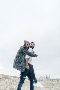 Low angle view of man giving piggyback to woman against sky