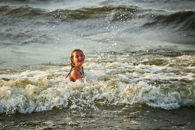 Low section of shirtless boy splashing water in sea