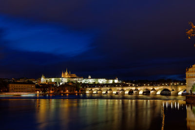 Illuminated buildings by river against sky at night