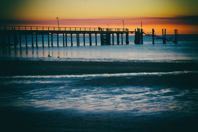 Silhouette wooden posts on beach against sky during sunset