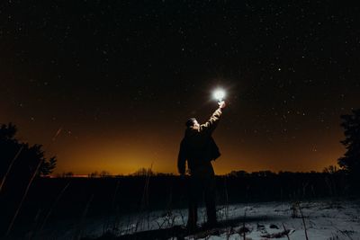 Silhouette man standing on snow against sky at night