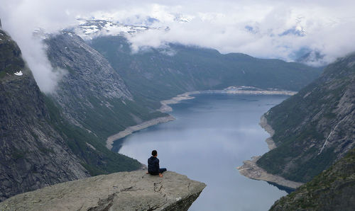 Rear view of man sitting on rock by mountains