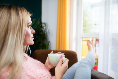 A young woman holds a cup and looks ahead.