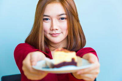 Portrait of woman holding cake in plate against wall