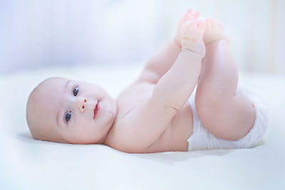 Portrait of shirtless cute baby boy lying on bed at home