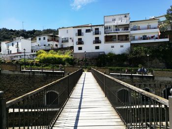 Footbridge over canal amidst buildings in city against sky