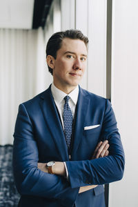 Portrait of confident businessman with arms crossed standing at workplace